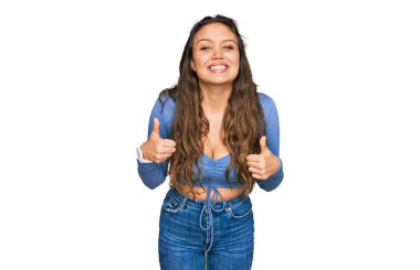 Gündelik kıyafetler giyen genç İspanyol kız. Başarı işareti ile el hareketi yapıyor. Gülümsüyor ve mutlu. Neşeli ifade ve kazanan jest. 