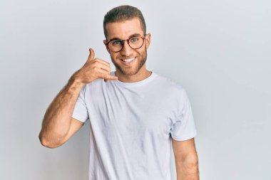 Gündelik kıyafetler ve gözlük takan genç beyaz adam telefonla el ve parmak hareketleriyle gülümsüyor telefonda konuşur gibi. iletişim kavramları. 