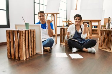Sanat stüdyosundaki genç İspanyol çift baş parmağını yana kaldırarak ağzı açık gülümsüyor. 
