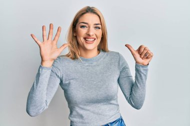 Gündelik giysiler giyen genç beyaz kadın altı numarayı gösterip işaret ederken kendinden emin ve mutlu gülümsüyor.. 