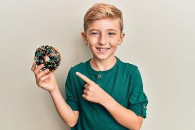 Küçük beyaz çocuk elinde çikolatalı donut tutarken mutlu bir şekilde elini ve parmağını gösterdi. 