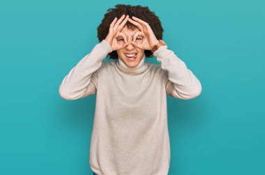 Kışın yün kazak giyen genç İspanyol kız dürbün gibi jest yapıyor, gözleri parmaklarından bakıyor. çılgın ifade. 