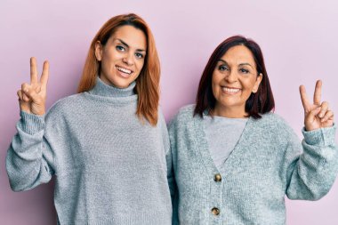 Latin anne ve kızı, sıradan kıyafetler giyip kameraya bakıp zafer işareti yaparken parmaklarını gösteriyorlar. İki numara.. 