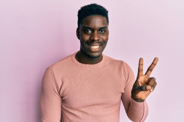 Yakışıklı, sıradan kıyafetler giyen, gülümseyen, kameraya göz kırpan, zafer işareti yapan siyahi bir adam. İki numara.. 