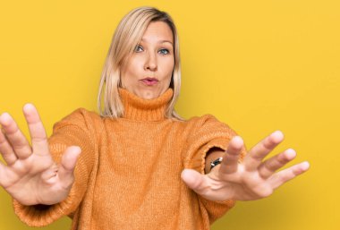 Orta yaşlı beyaz kadın, günlük kışlık süveter giyiyor. Avuç içi hareketlerini durduruyor. Öfkeli ve hayal kırıklığı dolu bir ifade takınıyor. 