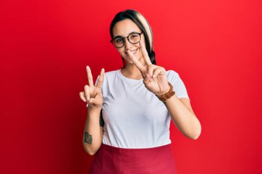 Profesyonel garson önlüğü giymiş genç İspanyol kadın kameraya bakıp zafer işareti yapıyor. İki numara.. 