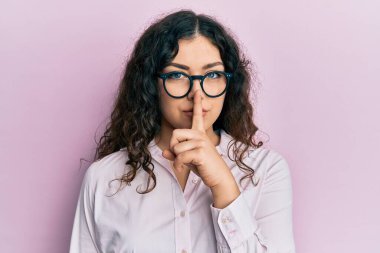 Kıvırcık saçlı, günlük kıyafetler giyen ve gözlüklü genç esmer kadın sessiz olmak istiyor. sessizlik ve gizli konsept. 