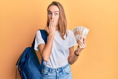 Öğrenci sırt çantası takan ve elinde 5000 Güney Koreli olan güzel sarışın kadın ağızlarını kapalı tutarak hata yapmaktan korktu ve şok oldu. şaşırmış ifade 
