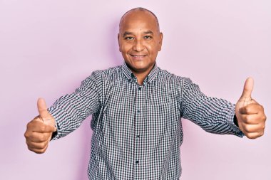 Orta yaşlı Latin bir adam gündelik giysiler giyip olumlu jestler yapıyor. Elleriyle gülümsüyor ve başarı için seviniyor. kazanan jest. 