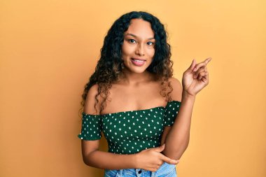 Gündelik kıyafetler giyen genç Latin kadın gülümsüyor mutlu bir şekilde elini ve parmağını yana uzatıyordu. 