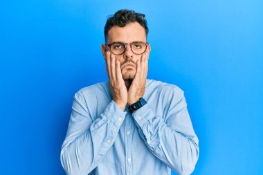 Gündelik kıyafetler ve gözlük takan genç İspanyol adam. Yüzü, depresyonu ve üzüntüyü örten yorgun eller. 