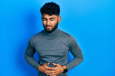 Arap sakallı bir adam boğazlı kazak giyiyor ve eli karnında çünkü hazımsızlık, acı verici bir hastalık kendini iyi hissetmiyor. Ağrı kavramı. 