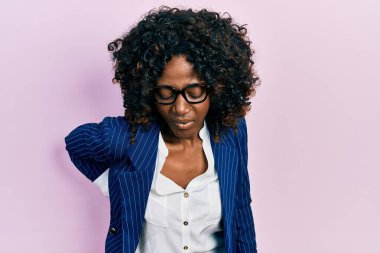 Genç Afrikalı Amerikalı kadın iş kıyafetleri ve gözlük takıyor sırt ağrısı çekiyor, elleriyle dokunuyor, kas ağrısı çekiyor. 