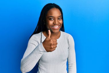 Saçları örgülü, beyaz süveter giyen, mutlu bir el hareketi yapan Afro-Amerikan kadın. Kameraya bakıp başarıyı gösteren ifade. 