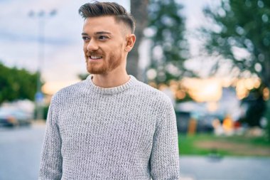 Genç beyaz adam gülümseyerek şehirde mutlu mesut duruyor..