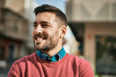 Genç İspanyol adam gülümseyerek şehirde mutlu mesut dikiliyor..