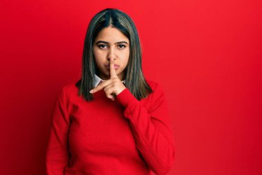 Gündelik giysiler giyen genç Latin kadın parmakları dudaklarında sessiz olmak istiyor. sessizlik ve gizli konsept. 