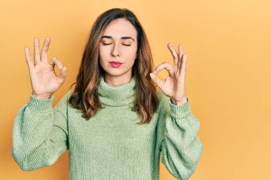 Gündelik kıyafetler giyen, gözleri kapalı gülümseyen genç İspanyol kız parmaklarıyla meditasyon hareketi yapıyor. yoga konsepti. 