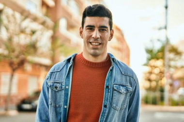 Genç İspanyol adam gülümseyerek şehirde mutlu mesut dikiliyor..