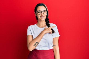 Genç İspanyol kadın profesyonel garson önlüğü giyiyor. Neşeli. Yüzünde mutlu ve doğal bir ifadeyle elleri ve parmaklarıyla yüzünü gösteren bir gülümseme var. 