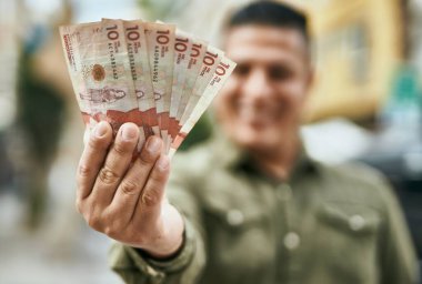 Genç Latin adam gülümsüyor. Şehirde elinde Kolombiya pezosu var..