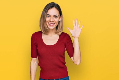 Genç sarışın kız gündelik giysiler giyer ve beş numarayı göstererek gülümserken kendinden emin ve mutluydu.. 