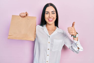 Mavi gözlü güzel bir kadın elinde paket kağıdı, mutlu ve pozitif gülümsüyor, başparmağı mükemmel ve onay işareti yapıyor. 