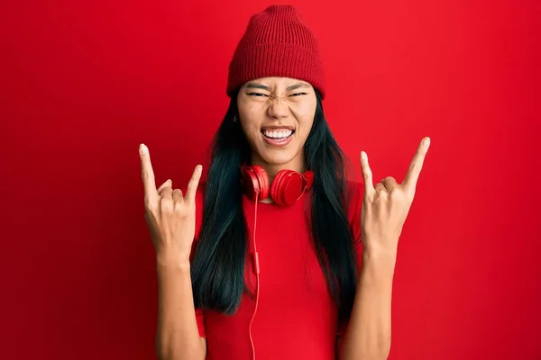 年轻的中国女人用耳机听音乐 用疯狂的表情用双手做摇滚符号 音乐明星 沉重的概念 — 图库照片