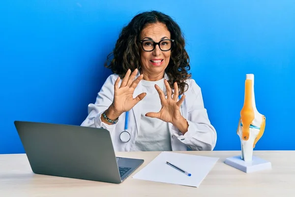 Beautiful middle age woman doctor at orthopedic clinic disgusted expression, displeased and fearful doing disgust face because aversion reaction. with hands raised