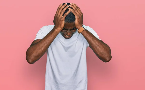 痛みや片頭痛のため 頭痛が絶望的でストレスを受けたカジュアルな白いTシャツを着た若いアフリカ系アメリカ人男性 手を頭に — ストック写真