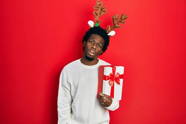 Jovem Afro Americano Vestindo Chapéu Natal Veado Segurando Presente Olhando — Fotografia de Stock