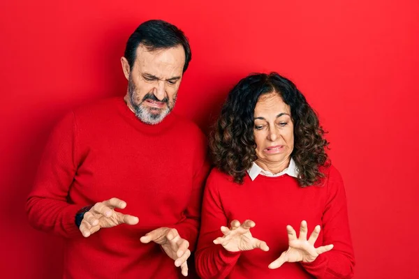 Middle age couple of hispanic woman and man hugging and standing together disgusted expression, displeased and fearful doing disgust face because aversion reaction.