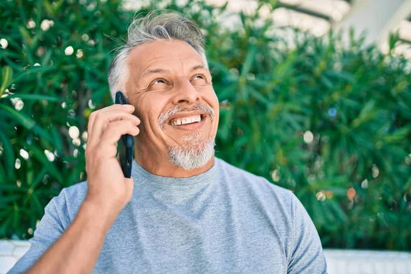 中年时 他惊慌失措的头发灰白的男人高兴地在公园里用智能手机聊天 — 图库照片