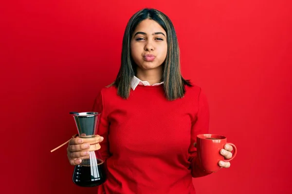 年轻的拉丁女人 手里拿着咖啡滤嘴和茶杯 脸上带着滑稽的表情 嘴被空气吹胀 — 图库照片