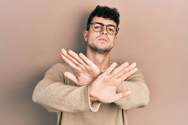 カジュアルな服と眼鏡の拒絶表現を身に着けている若いヒスパニック系の男交差腕と手のひら負の記号を行う 怒っている顔 — ストック写真