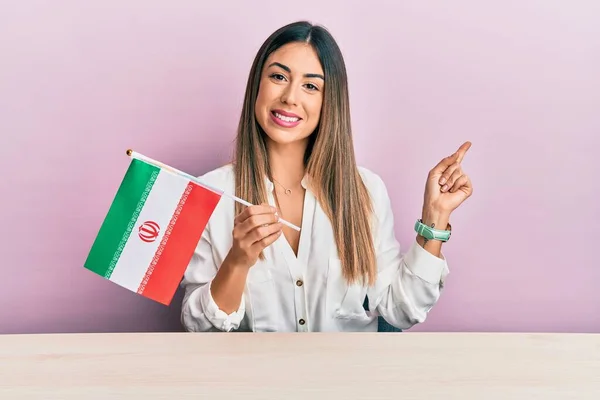 Jovem Hispânica Segurando Bandeira Irã Sentada Mesa Sorrindo Feliz Apontando — Fotografia de Stock