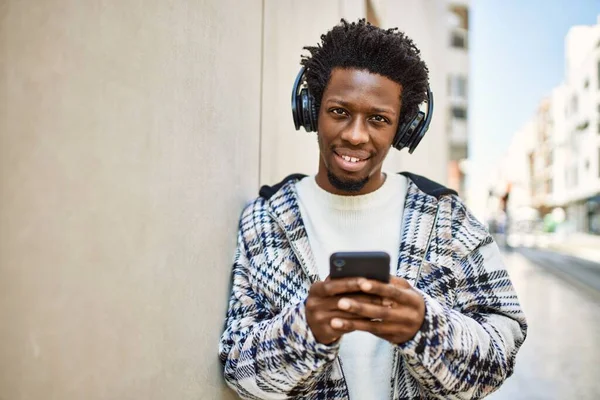 ヘッドフォンを着用し スマートフォンを使用して音楽を聴くアフロ髪のハンサムな黒人男性 — ストック写真