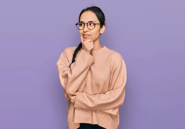若いヒスパニック系の女の子の質問について考えて顎に手でカジュアルな服や眼鏡を着用し 包括的な表現 思慮深い顔で笑顔 疑わしい概念 — ストック写真