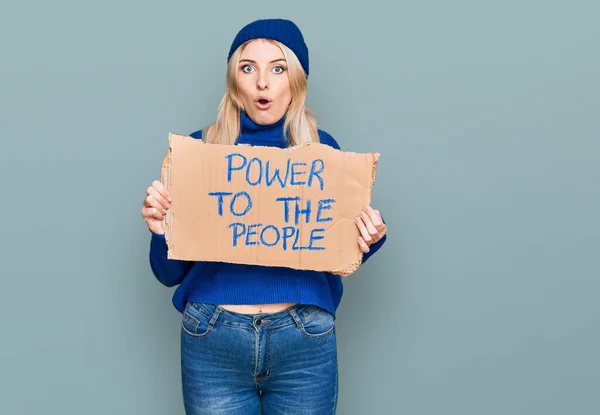 Young caucasian woman holding power to the people banner scared and amazed with open mouth for surprise, disbelief face