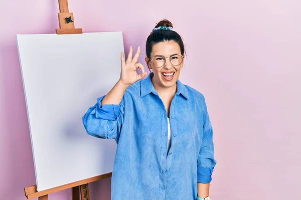 画家のイーゼルのそばに立つ若いヒスパニック系の女性は 手と指でOkサインを行う積極的な笑顔立っている 成功した表現 — ストック写真