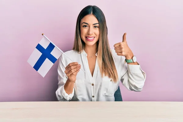 Молодая Латиноамериканка Финским Флагом Сидит Столе Улыбаясь Счастливой Позитивной Большой — стоковое фото