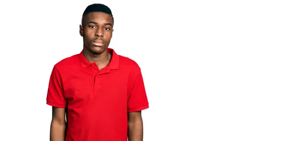 カジュアルな赤いTシャツを着た若いアフリカ系アメリカ人男性が 真剣な表情でリラックスしています カメラを見ているだけで — ストック写真