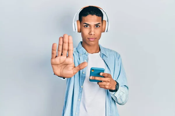 Joven Afroamericano Chico Usando Teléfono Inteligente Con Auriculares Con Mano —  Fotos de Stock