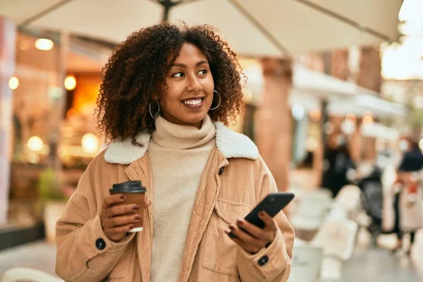 アフリカ系アメリカ人の若い女性が市内でスマートフォンやコーヒーを飲んでいる — ストック写真