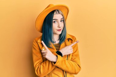 Sarı şapkalı ve deri ceketli genç modern kız parmaklarıyla her iki tarafı işaret ediyor, farklı yönlere bakıyor. 