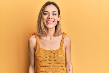 Yüzünde mutlu ve havalı bir gülümseme olan günlük sarı tişört giyen beyaz bir kadın. şanslı kişi. 