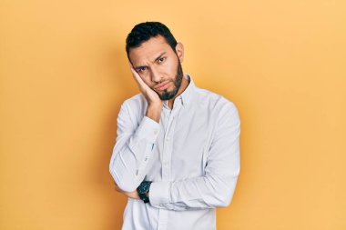 Sakallı, iş gömleği giyen İspanyol bir adam kollarını kavuşturarak depresyondan sıkılmış ve yorgun göründüğünü düşünüyor.. 