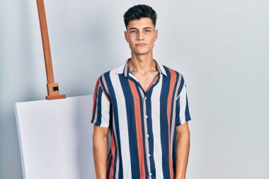 Boş tuvale yakın duran genç İspanyol adam yüzünde ciddi bir ifadeyle rahatladı. Basit ve doğal bir şekilde kameraya bakıyorsun.. 