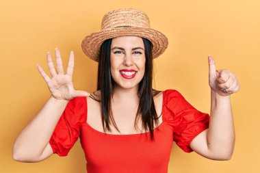 Genç İspanyol kadın yaz şapkası takıyor. Altıncı parmaklarını gösterip işaret ederken kendinden emin ve mutlu bir şekilde gülümsüyor.. 