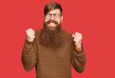 Genç İrlandalı kızıl elbiseli ve gözlüklü adam başarı için heyecanlı kolları havada ve gözleri kapalı zaferi kutlarken gülümsüyor. Kazanan konsept. 